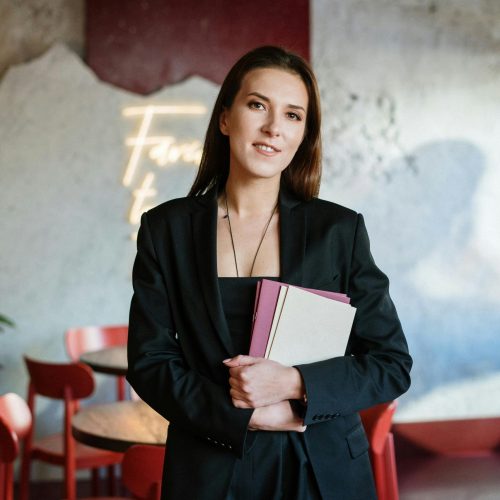 A young woman in a stylish café holding a menu, exuding confidence amidst a chic interior.